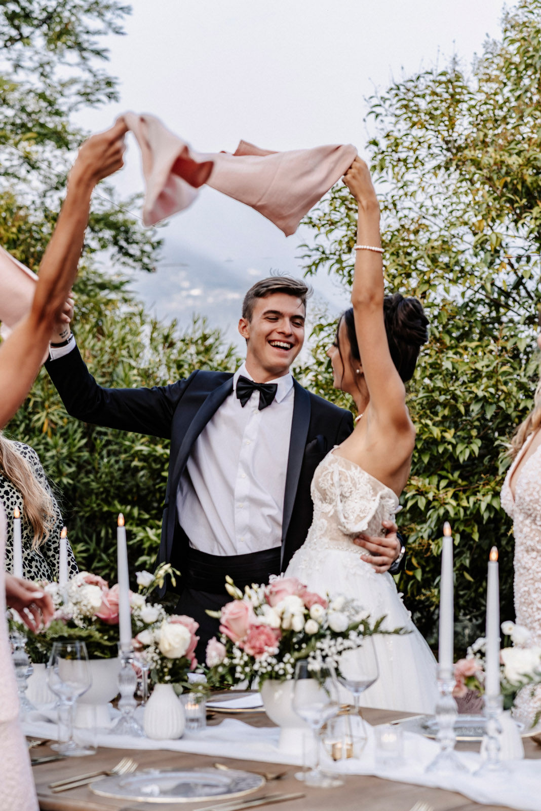 Guests waving napkins over the couple at an outdoor dinner with a lake view