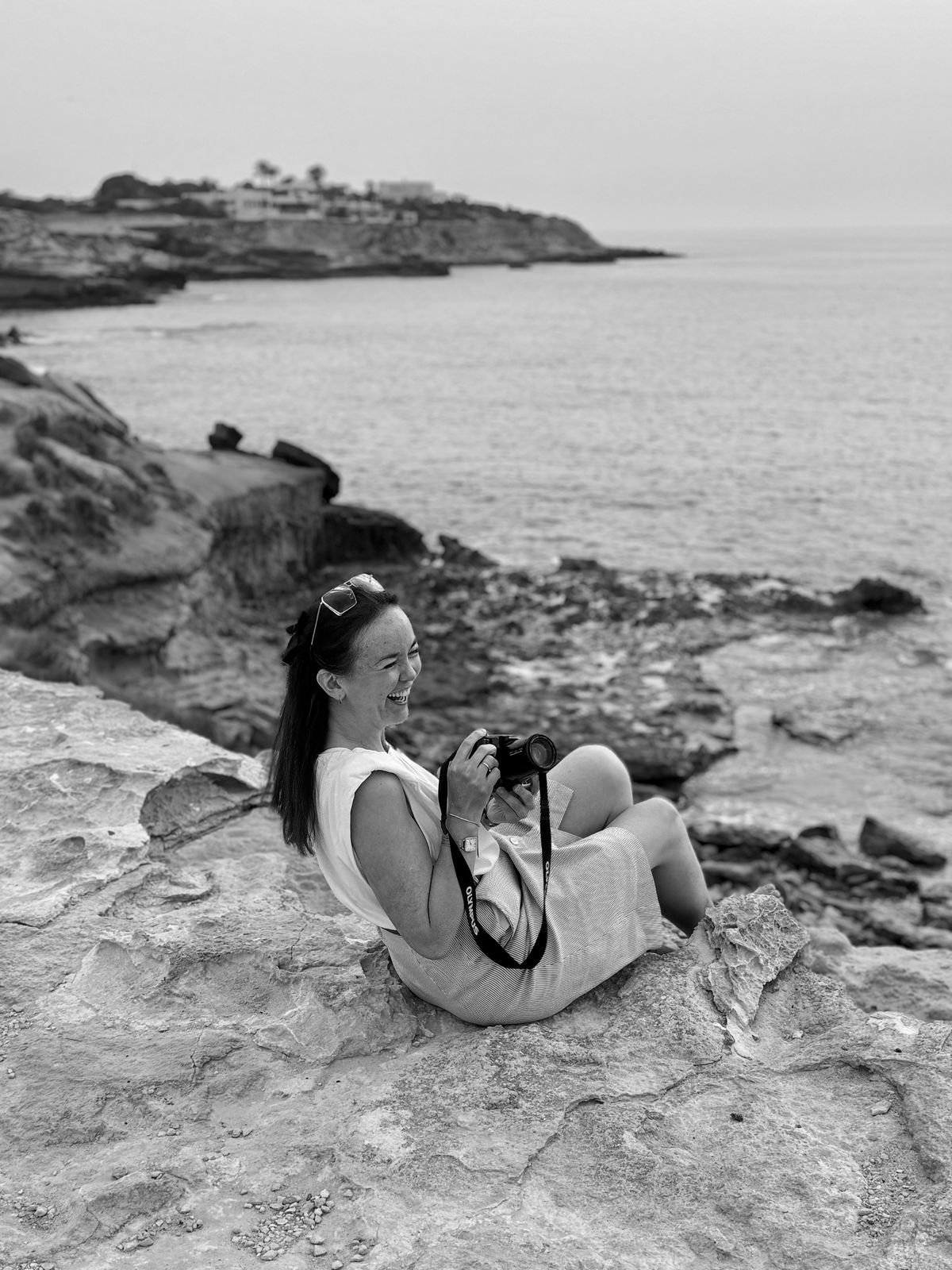 Greta Kurt laughing on a rocky coastline, camera in hand