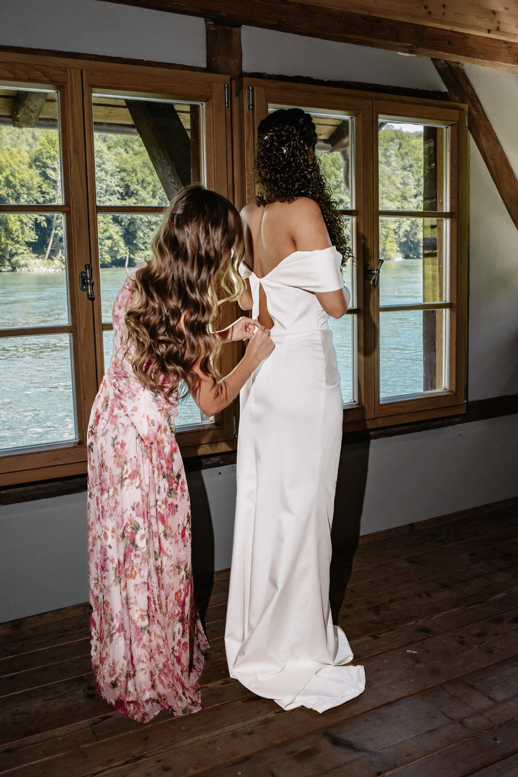 The wedding dress being fastened in front of a window overlooking the Rhine