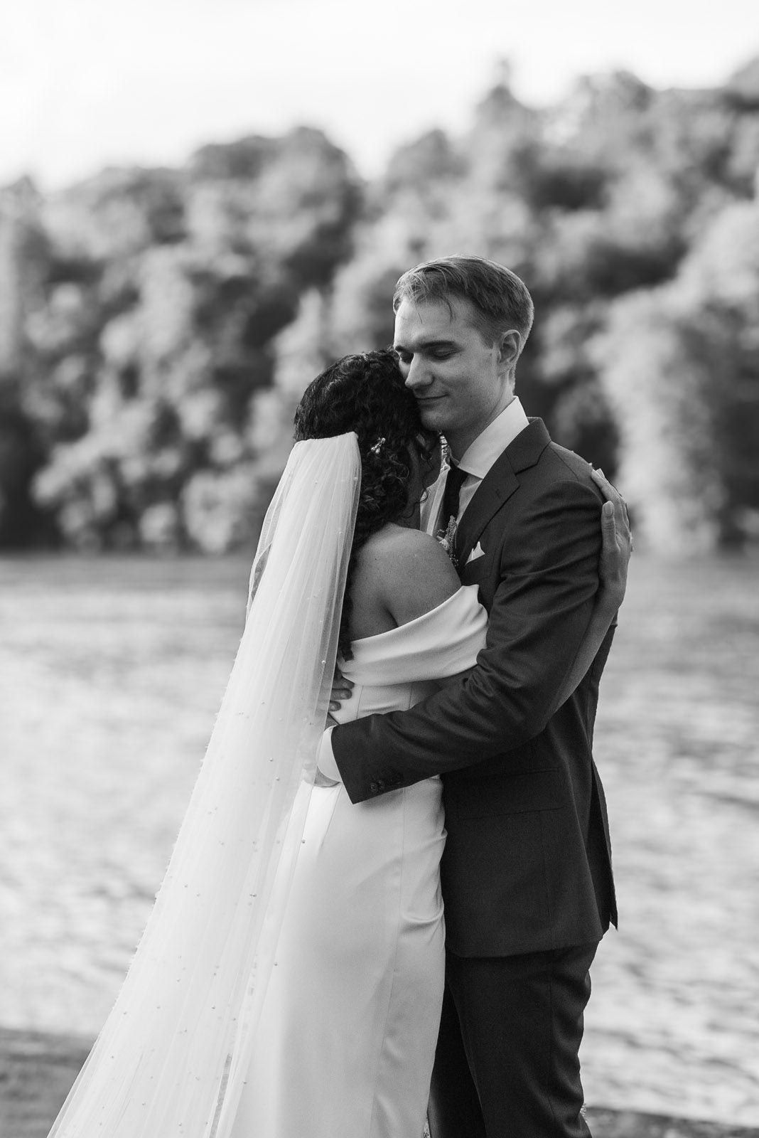 The couple holding each other quietly by the water, away from the guests