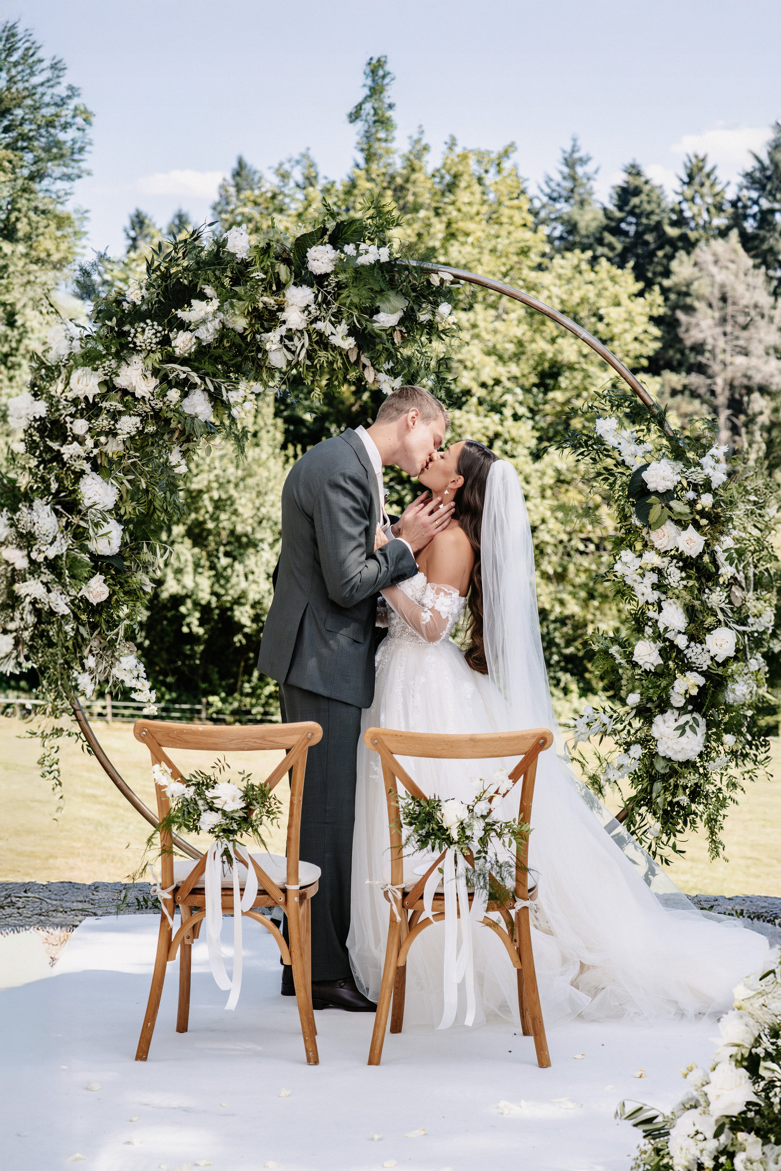 Nadine and Nick kissing under a circular flower arch at their outdoor ceremony at Hoher Darsberg